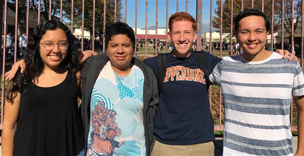 Photo of four high school students standing in front of a gate: a femal, and three males